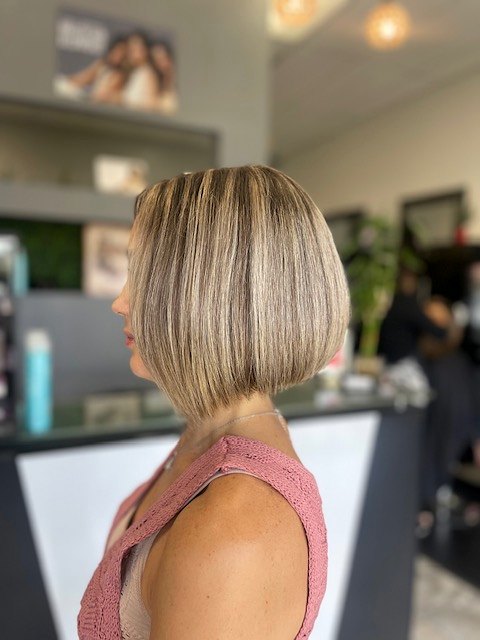 Sleek chin-length bob with soft blonde highlights, seen from the side in the salon