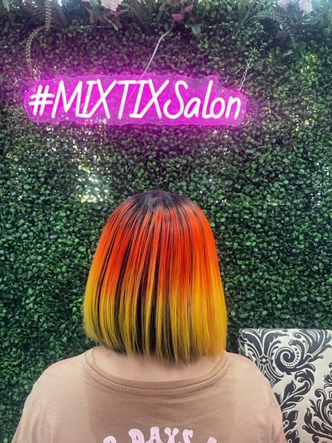 Short bob colored from deep red to bright yellow, in front of the salon's pink #MIXTIXSalon neon sign